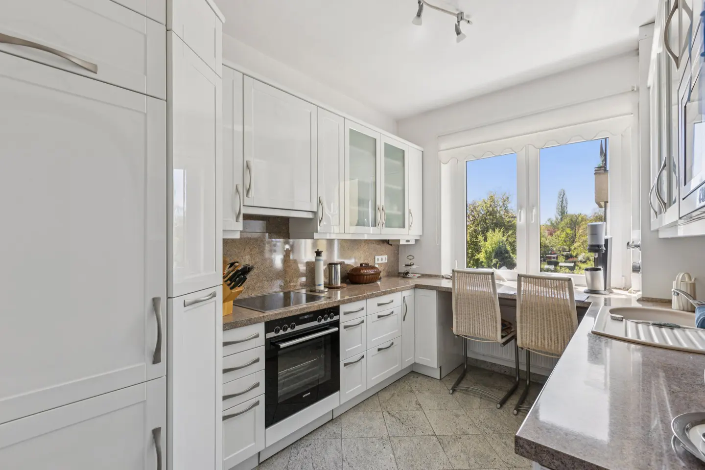 Bright kitchen with white cabinets, granite countertops, and stainless steel appliances. A window overlooks a green outdoor space.