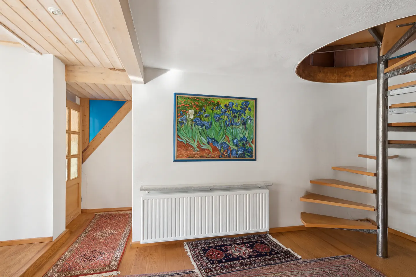 Interior view of a room with wooden floors, a spiral staircase, and a painting of irises on the wall.