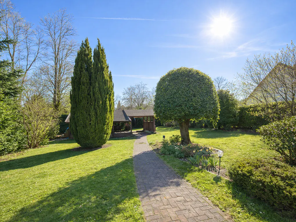A brick path leads to a gazebo in a green lawn with trees under a sunny blue sky.