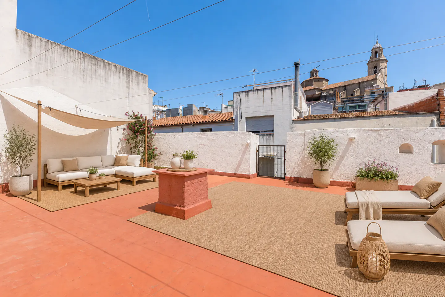 Sunny rooftop terrace with white walls, terracotta floor, lounge seating, sun shade, and views of a historic church tower.