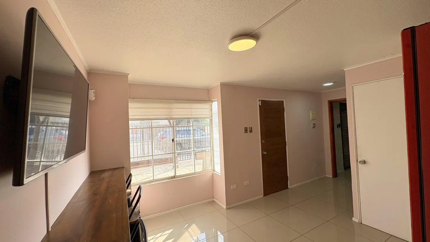 A bright living room with pink walls, a large window, a TV, and tile floors.