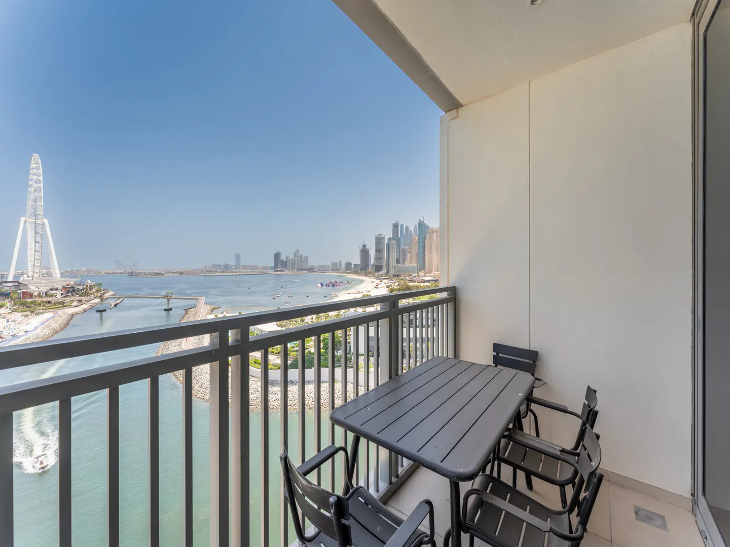 Balcony view of Dubai Eye and skyline. Gray table and chairs sit on the balcony overlooking the water and city.