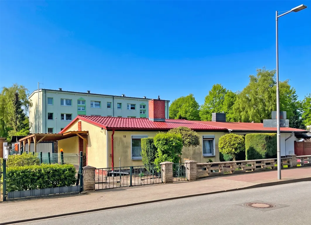 A one-story yellow house with a red roof and a black metal fence under a clear blue sky.