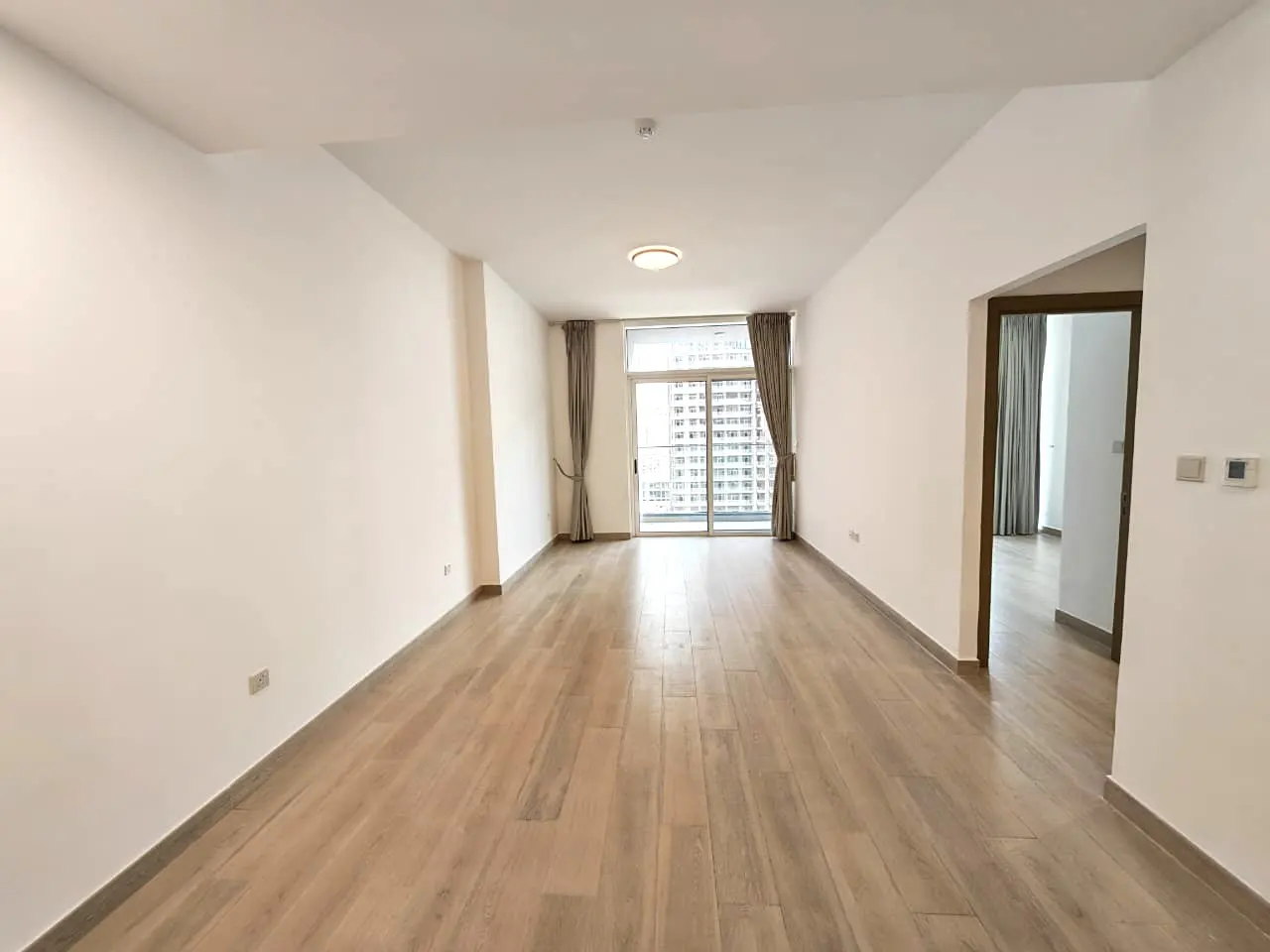 Unfurnished room with light wood floors, white walls, and a sliding glass door to a balcony with city views.