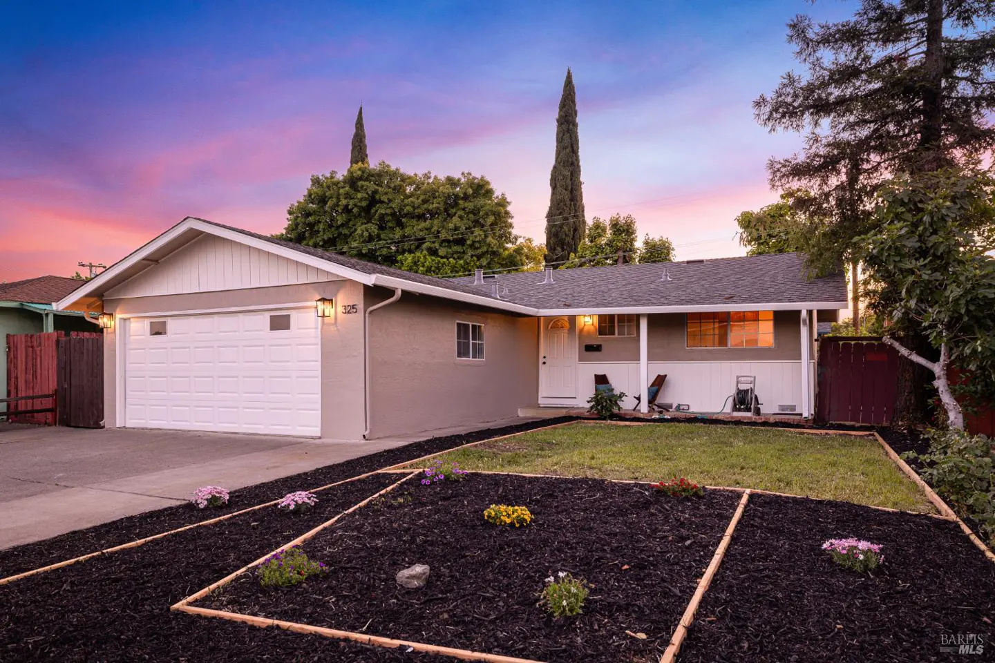 Front exterior of a single-story home with a white garage door, gray siding, and a manicured lawn at dusk.