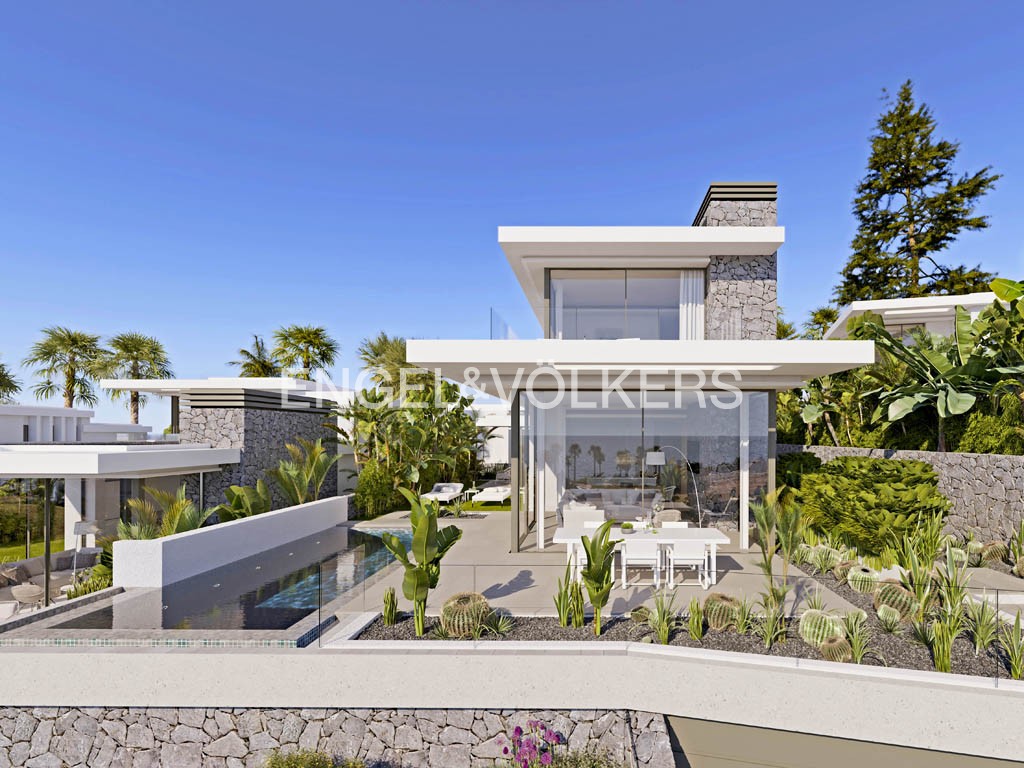 Modern villa with a pool, stone accents, and floor-to-ceiling windows under a clear blue sky. Palm trees and lush greenery surround the property.