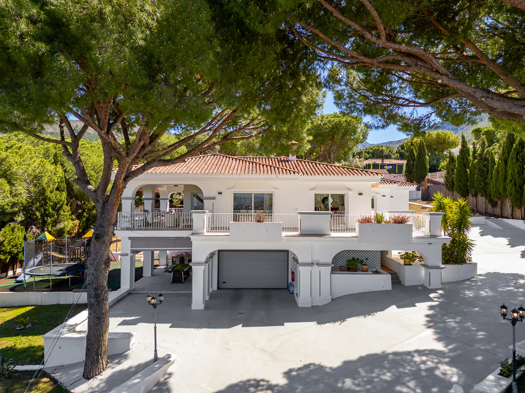 Two-story white house with a red tile roof, a gray garage door, and a large tree in the front yard.