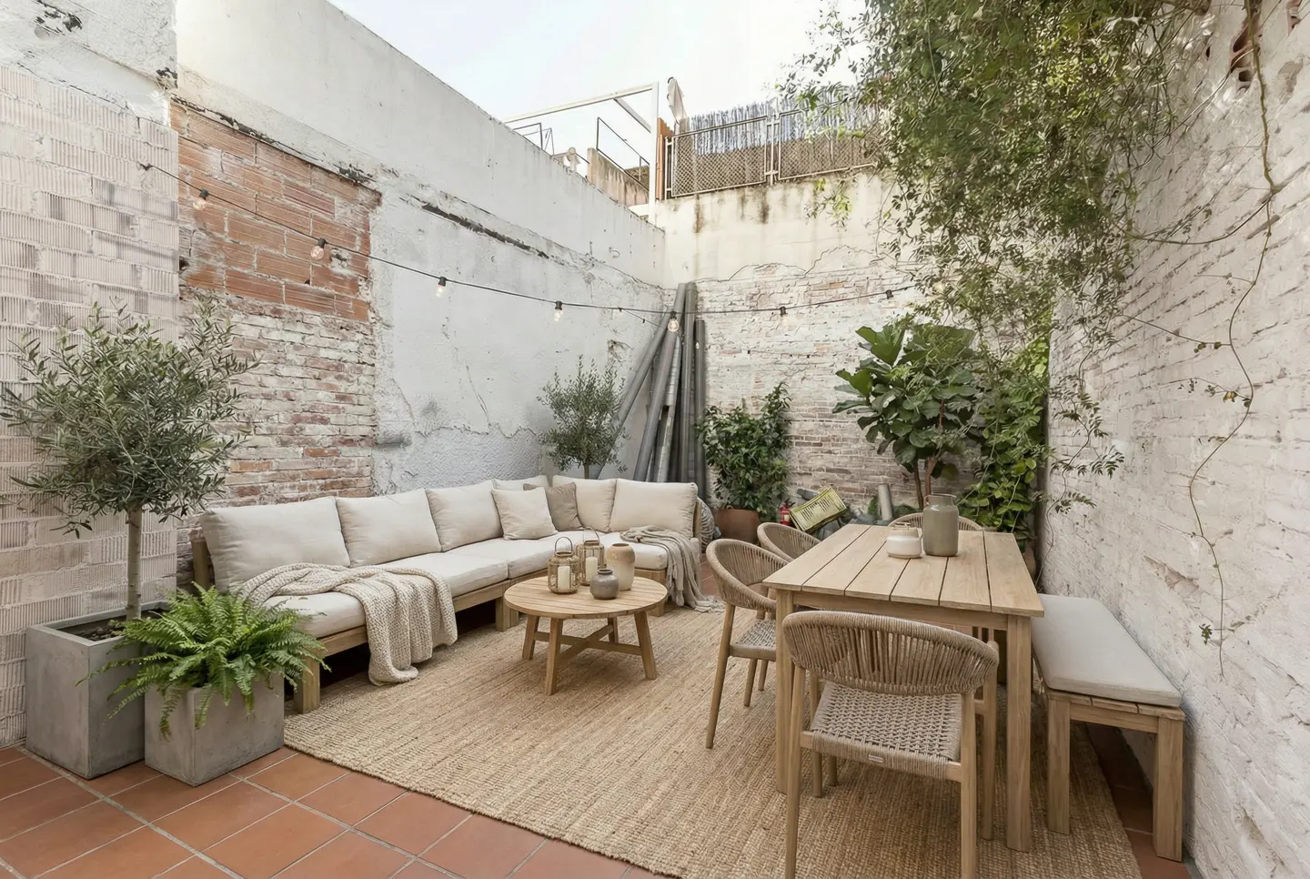 Outdoor patio with a wooden sectional sofa, table, chairs, and plants against a white brick wall.