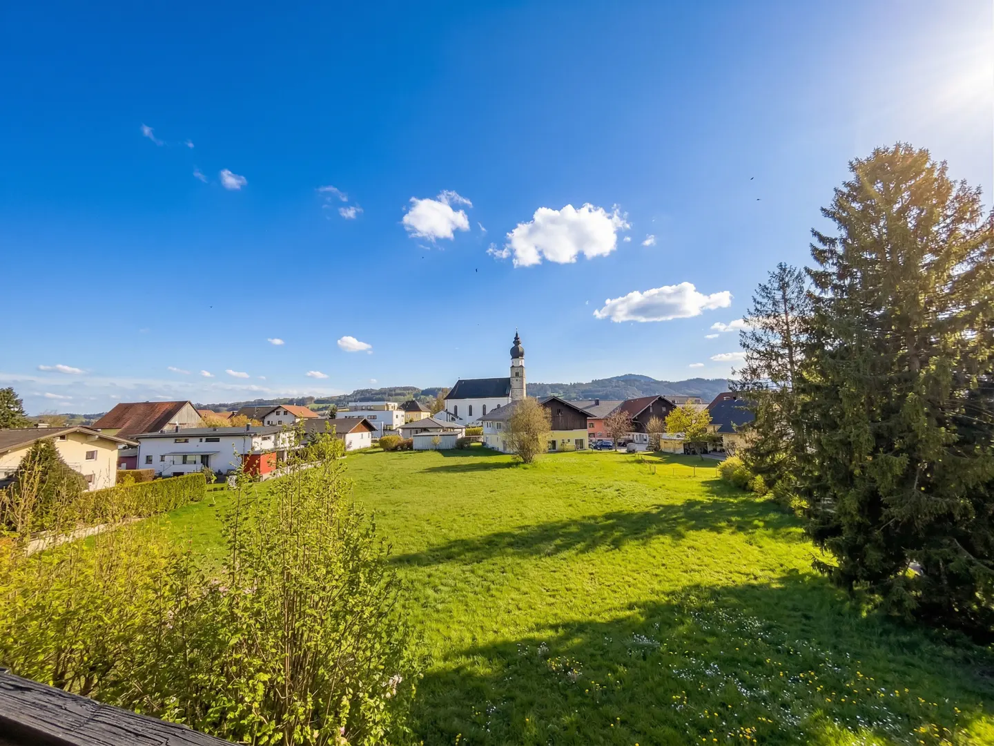 Scenic view of a village with a church, houses, and green fields under a blue sky with scattered clouds.