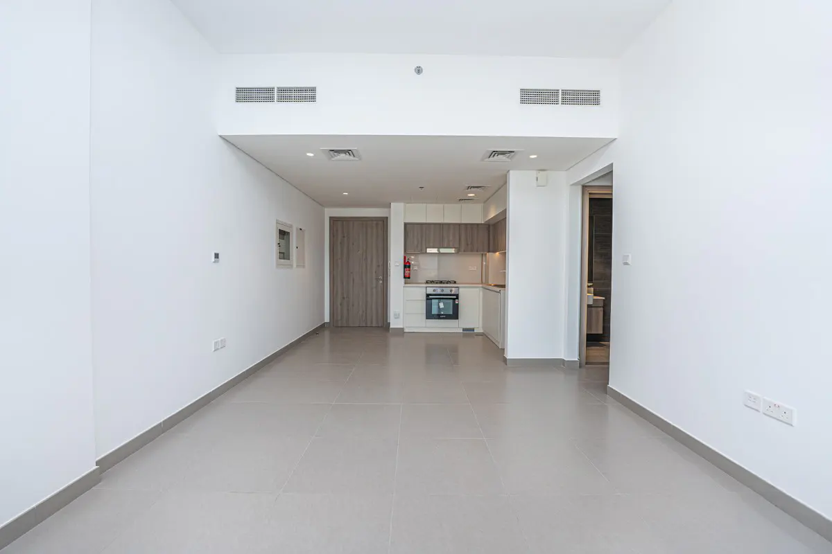 Modern, unfurnished apartment with white walls, light tile floors, and a compact kitchen with wood-toned cabinets.