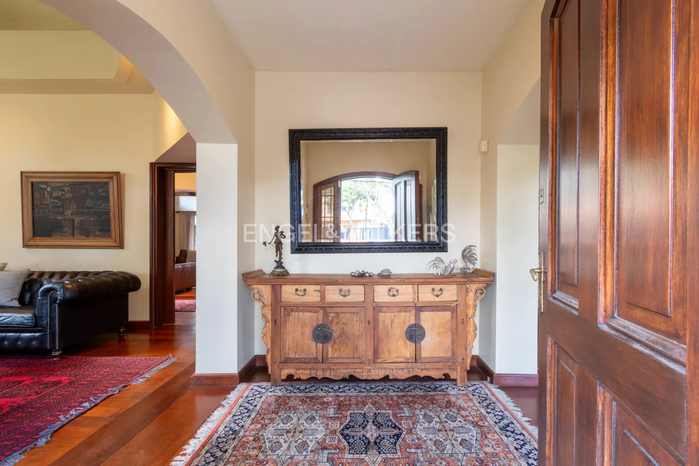 A foyer with a wooden console table, a black framed mirror, and a patterned rug. A dark wood door is ajar.
