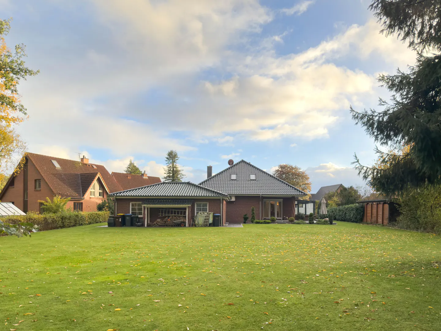 Backyard view of a brick house with a gray roof, a green lawn, and trees under a cloudy sky.
