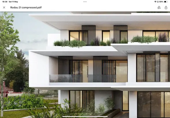 Modern white building with black window frames and vertical slats, surrounded by greenery.