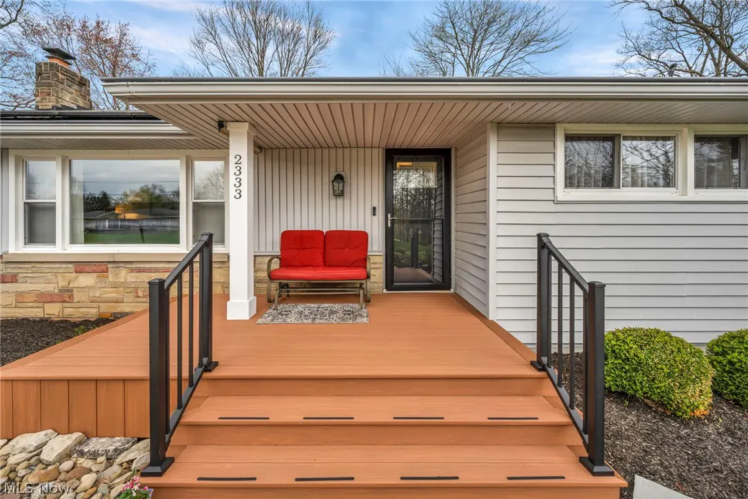 Front porch of a gray house with a red bench, black door, and brown deck with black railings. The house number "2333" is on a white column.