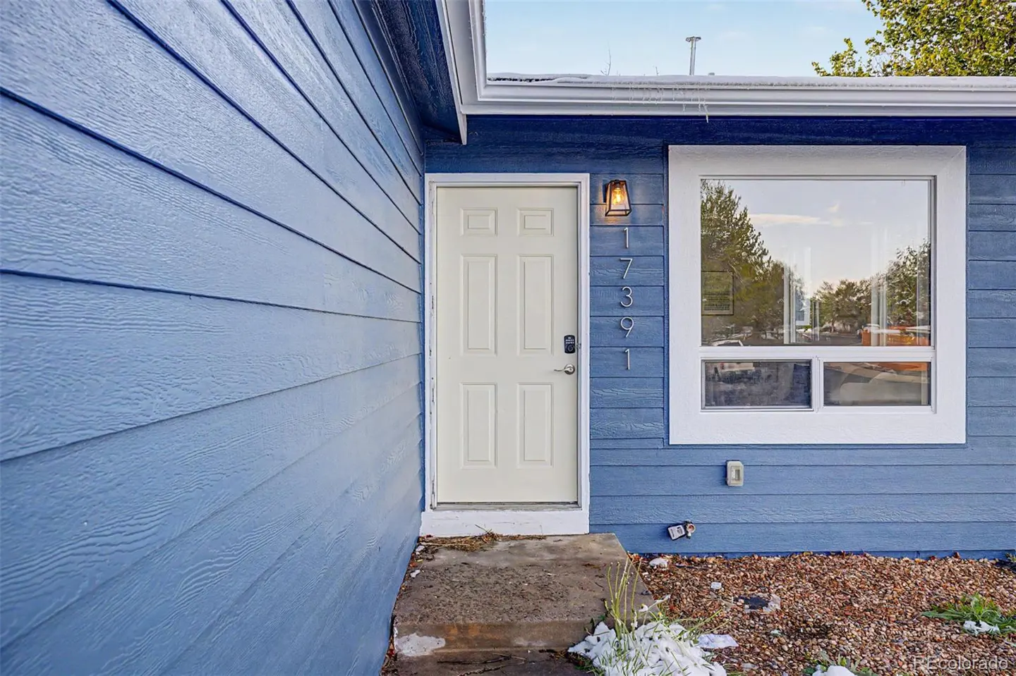 Exterior of a blue house with white trim, a white front door, and a window. The house number 17391 is displayed vertically.