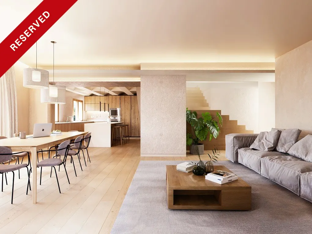 Open-concept living space with a dining table, kitchen, and gray sofa. A wooden coffee table sits on a gray rug. Stairs are visible in the background. "Reserved" banner.
