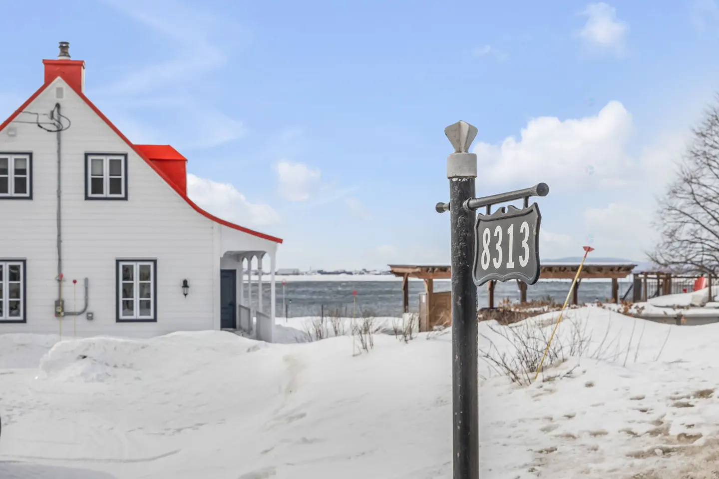White house with a red roof and a black address sign reading "8313" in a snowy landscape.