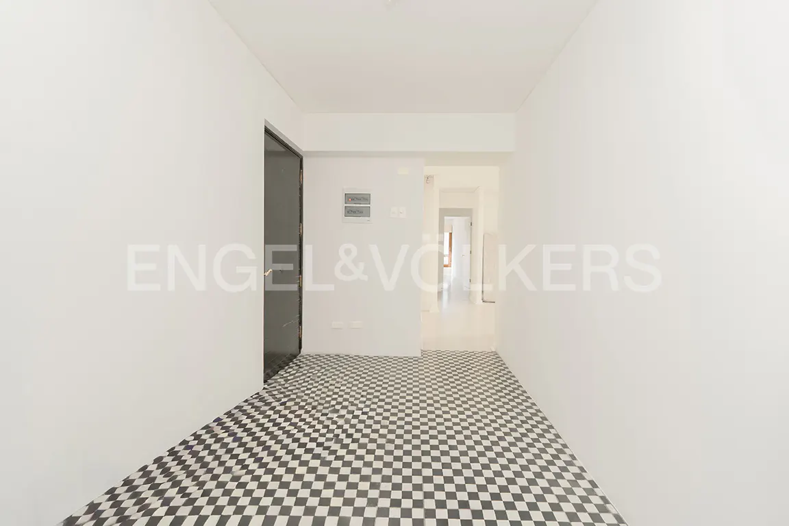 Bright hallway with white walls, black and white checkered tile floor, and a dark door leading to an interior corridor.