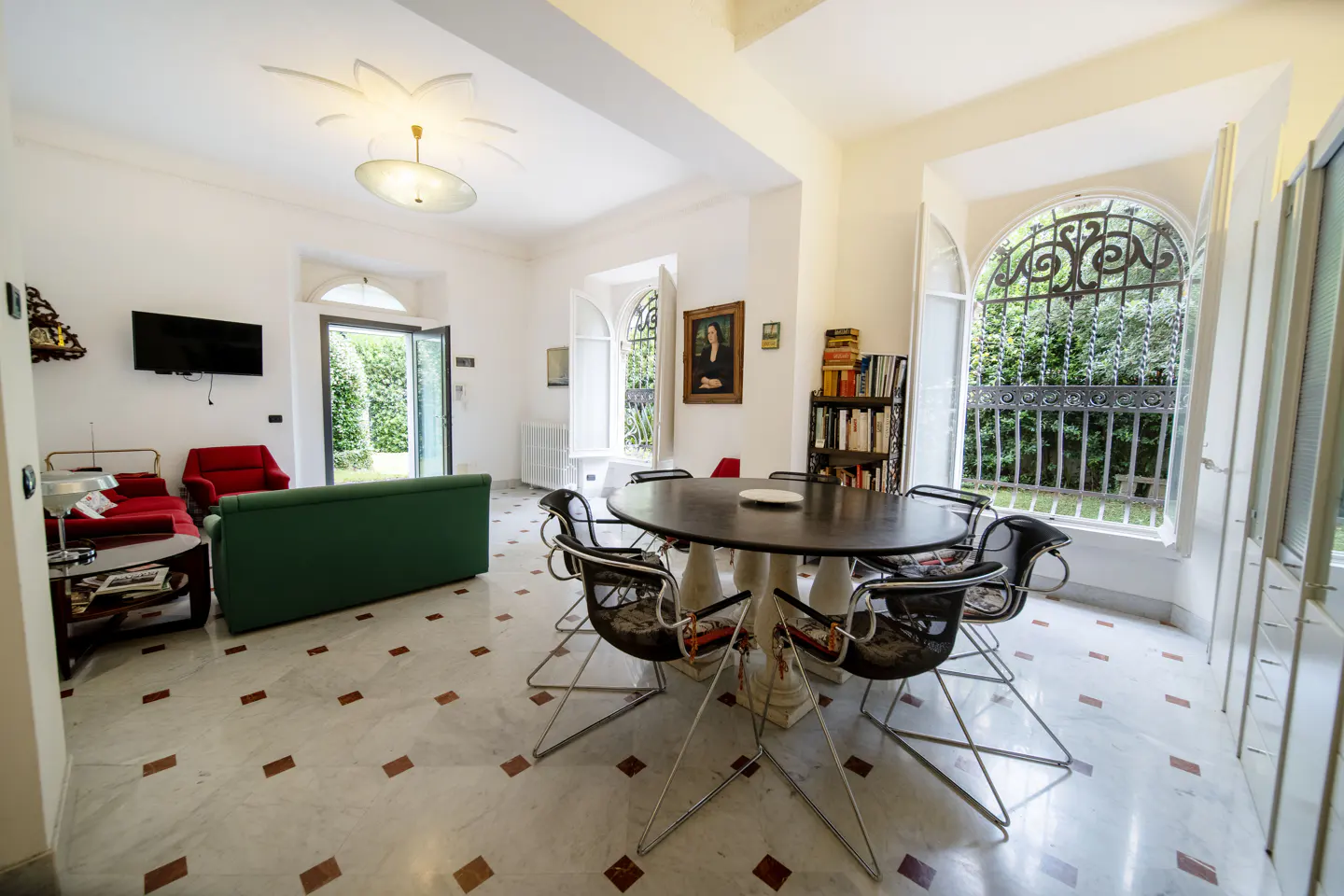 Bright living and dining room with marble floors, a green sofa, red chairs, and a round table with modern black chairs.