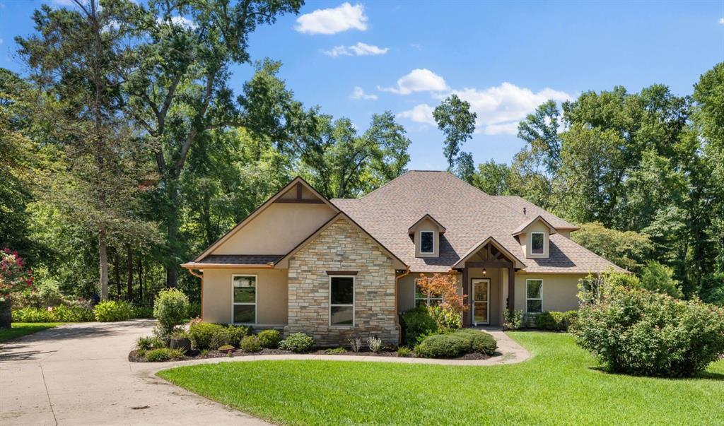 A tan stucco and stone house with a brown roof, surrounded by lush green trees and a manicured lawn under a blue sky. [AI-generated text]