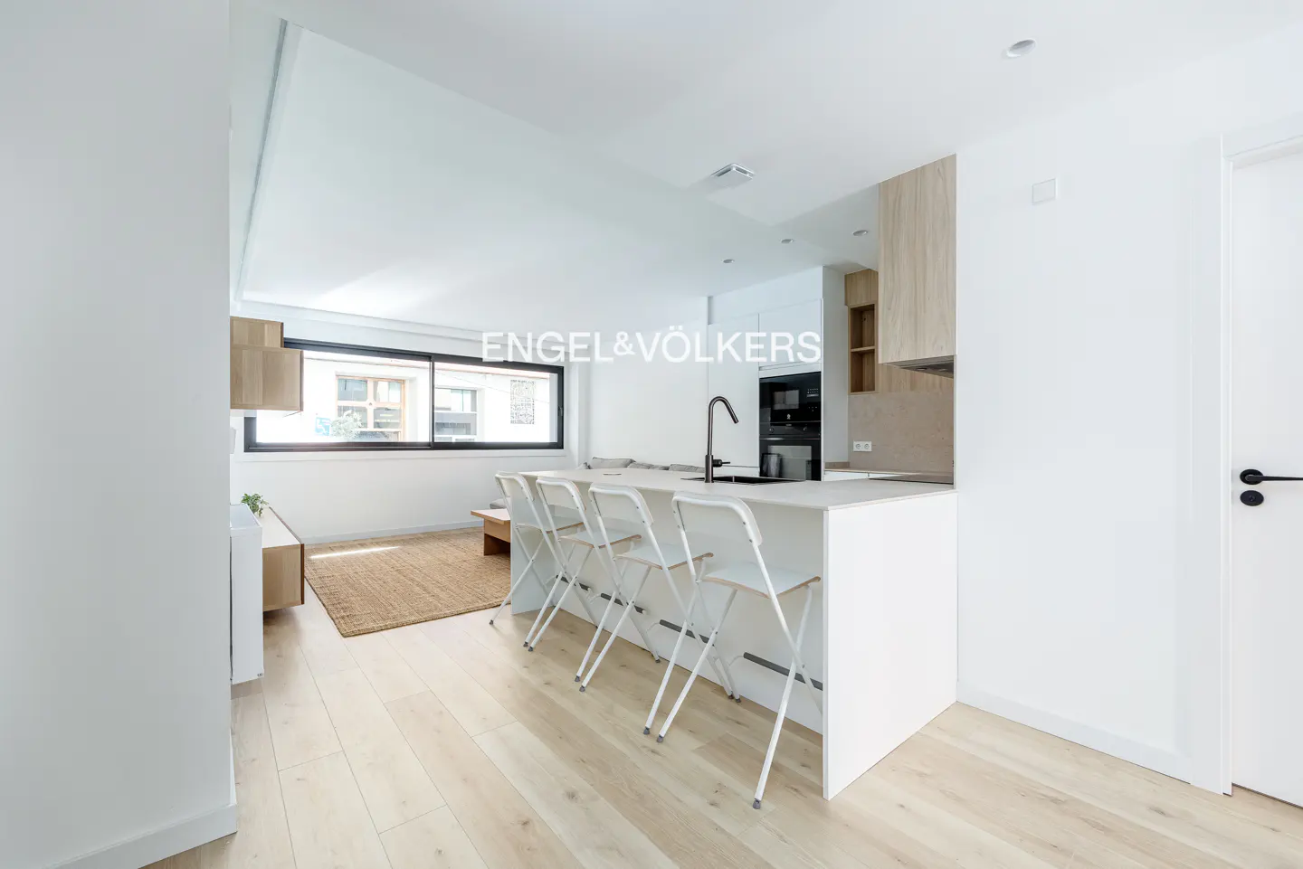 Modern open-plan kitchen with white island, three stools, light wood floors, and a living area with a jute rug.