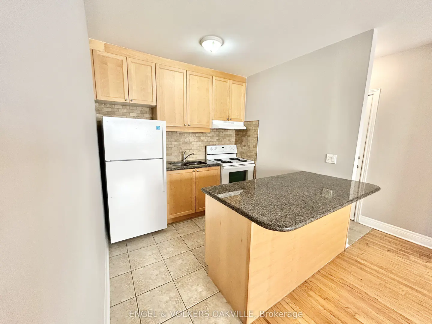 Kitchen with light wood cabinets, white appliances, granite-topped island, and tiled backsplash on a tile and wood floor.