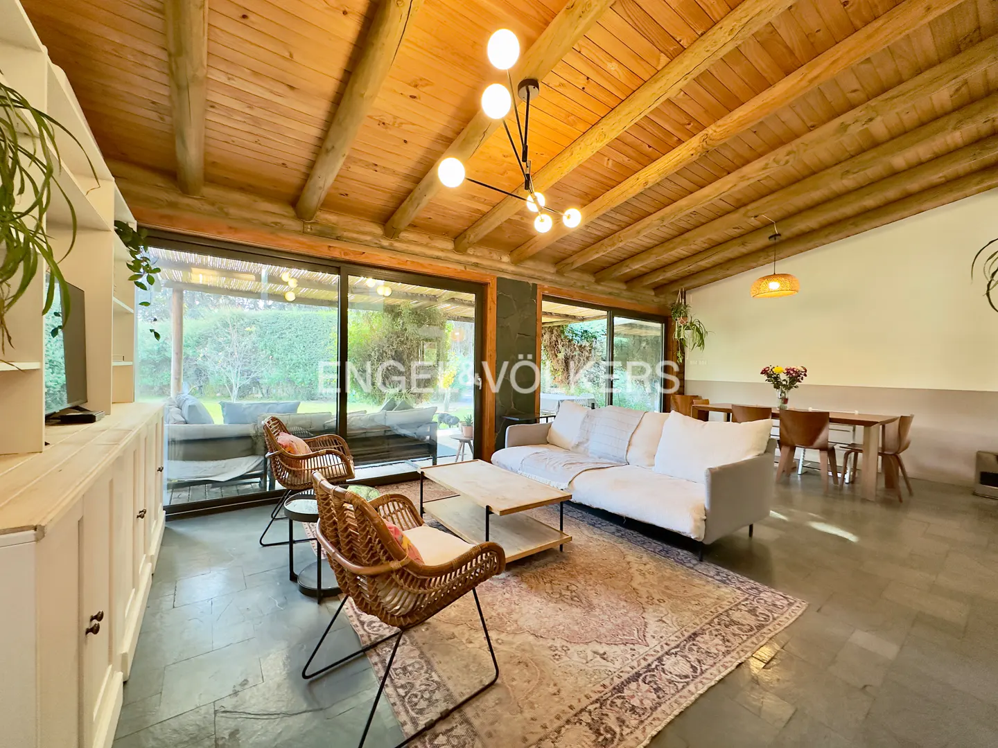 Living room with vaulted wood ceiling, white sofa, two rattan chairs, patterned rug, and large glass doors to the patio.