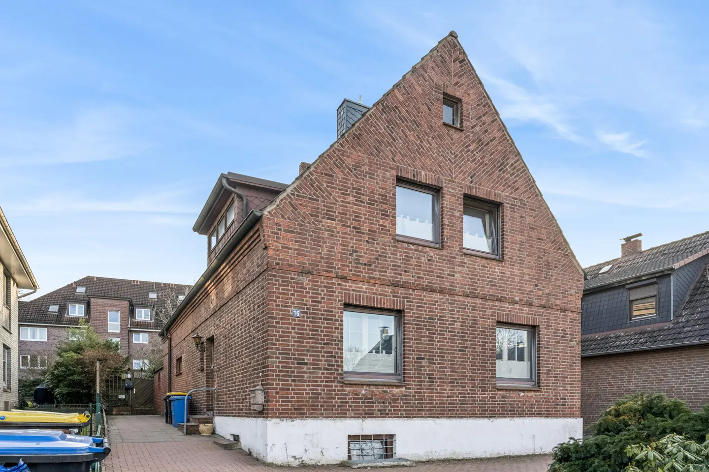 Exterior view of a three-story red brick house with a gabled roof and several windows under a blue sky.