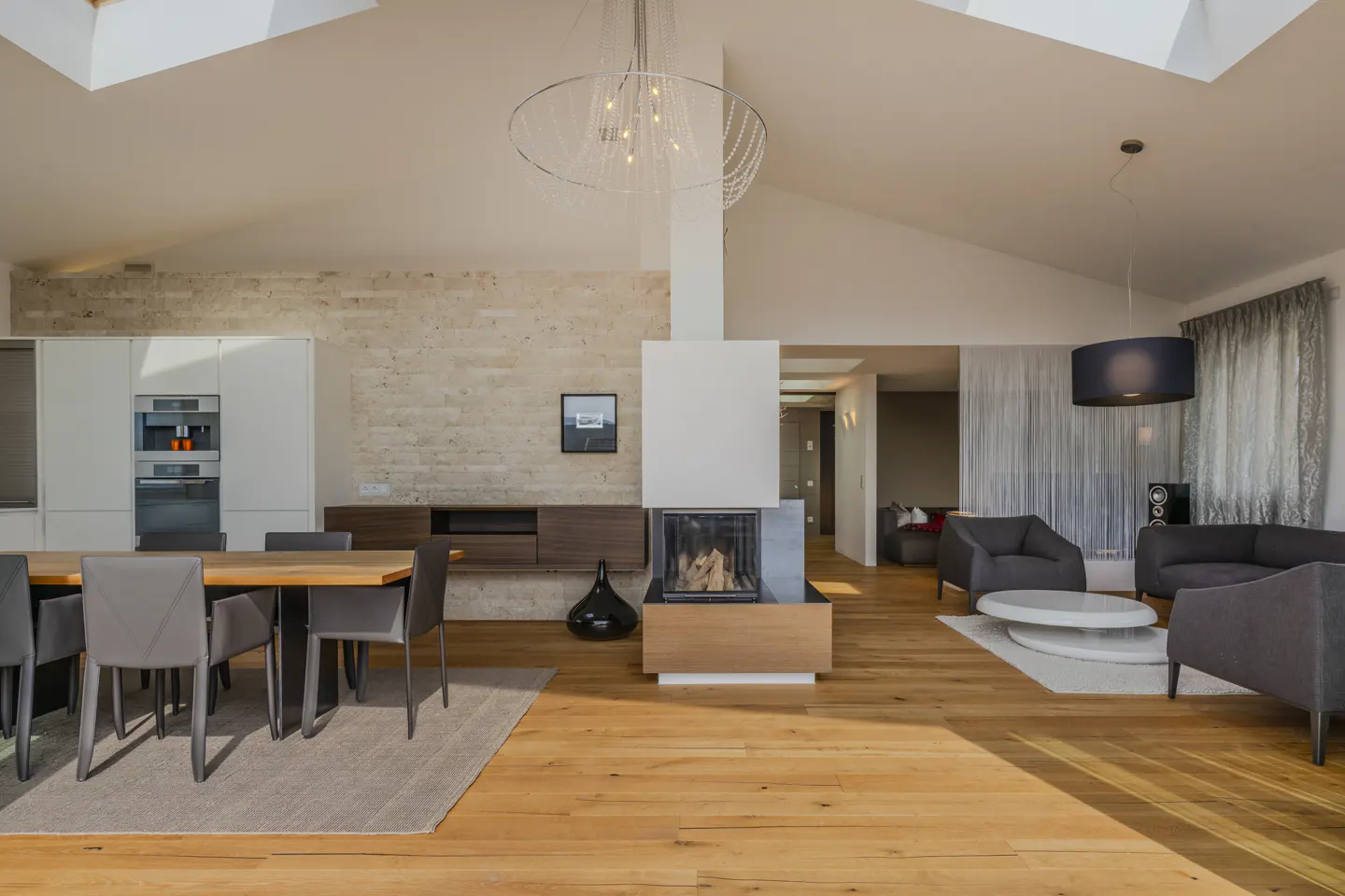 Bright, open-concept living space with wood floors, a dining table, and a modern fireplace. Gray seating area in the background.