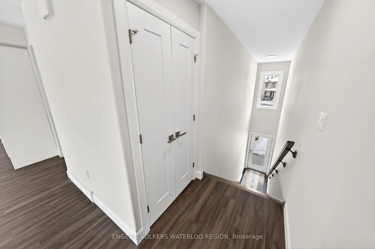 Bright hallway with white walls, dark wood floors, and a white closet. Stairs lead down to a door with a window above.