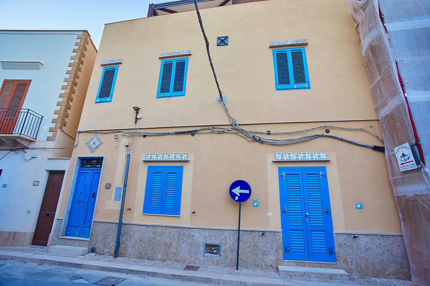 Two-story tan building with blue shutters and doors. A blue left-turn sign is in front of the building.