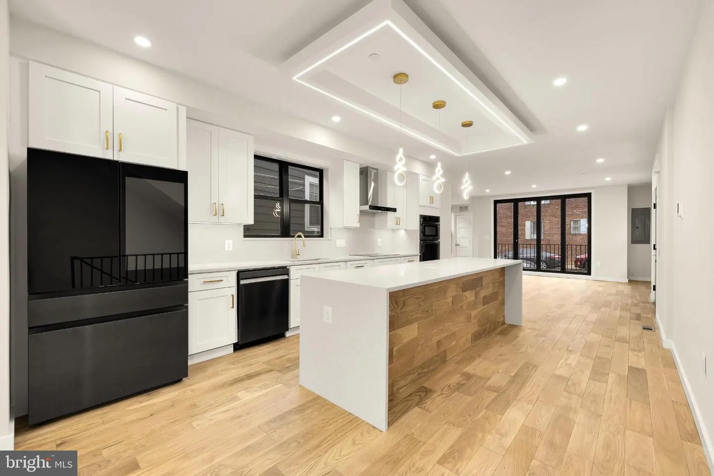 Bright, modern kitchen with white cabinets, black appliances, wood floors, and a center island with wood paneling.