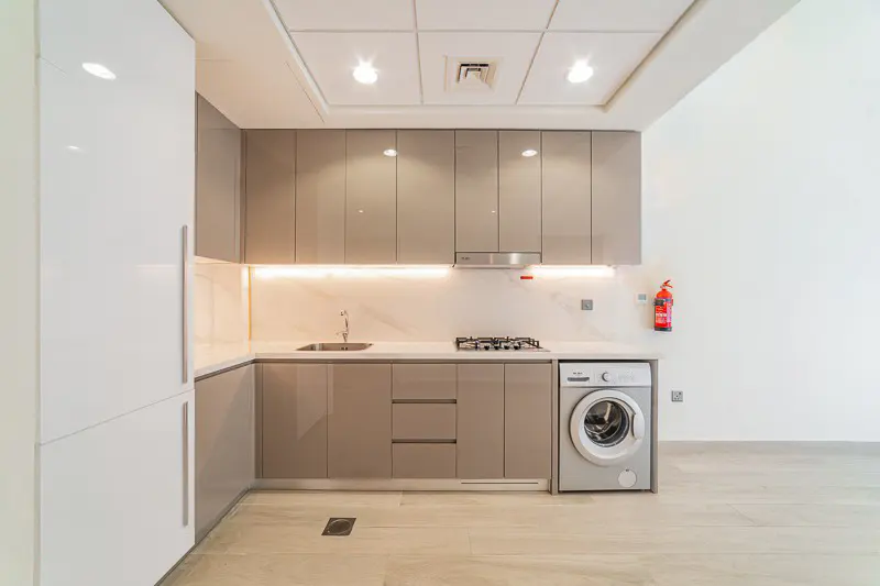 Modern kitchen with glossy taupe cabinets, white countertops, built-in washing machine, and recessed ceiling lighting.