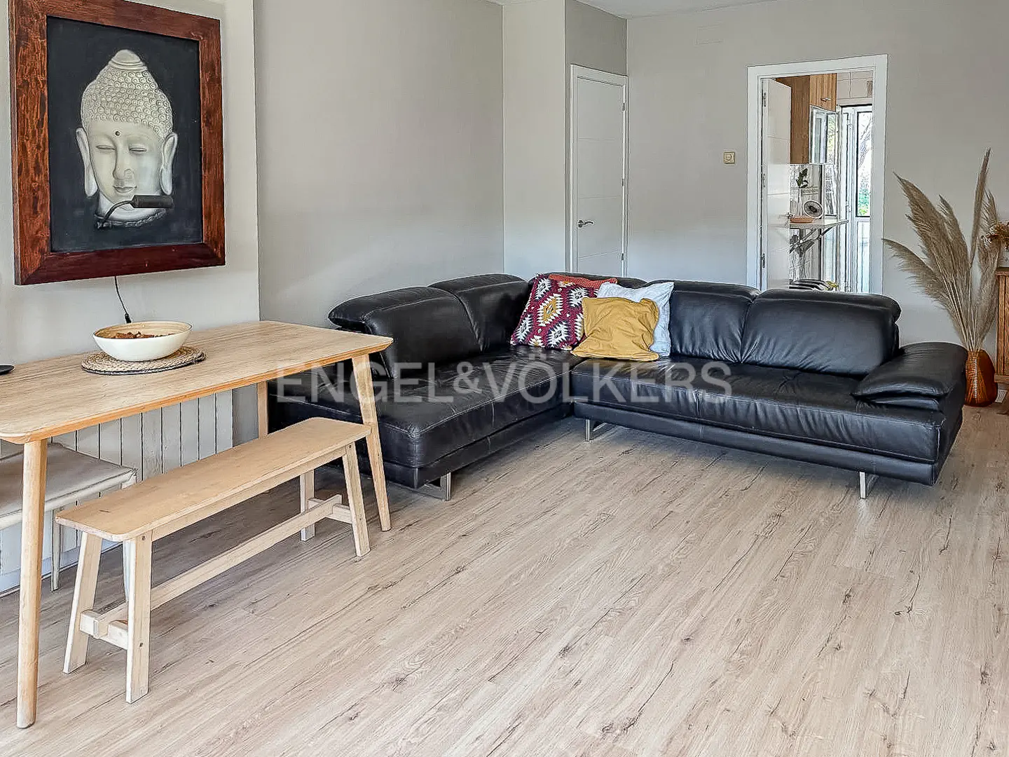 Living room with a black leather sectional sofa, wooden table with bench, and Buddha art on the wall.