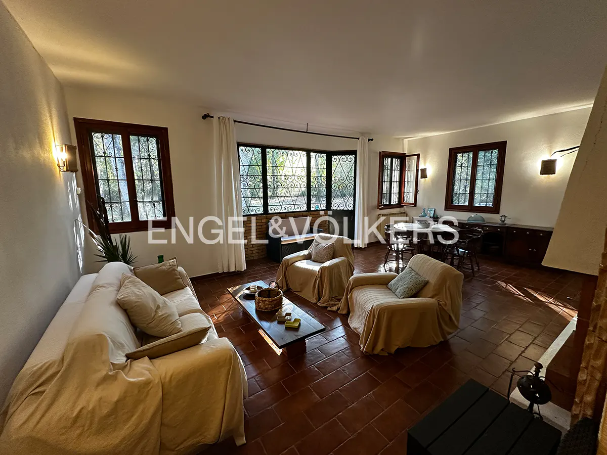 Spacious living room with terracotta tile floors, beige slipcovered furniture, a coffee table, and large windows.