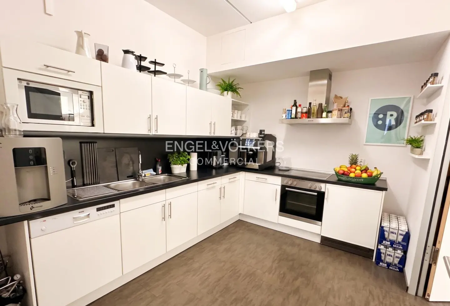 Bright kitchen with white cabinets, black countertops, and stainless steel appliances. Fruit bowl and beer cases add pops of color.