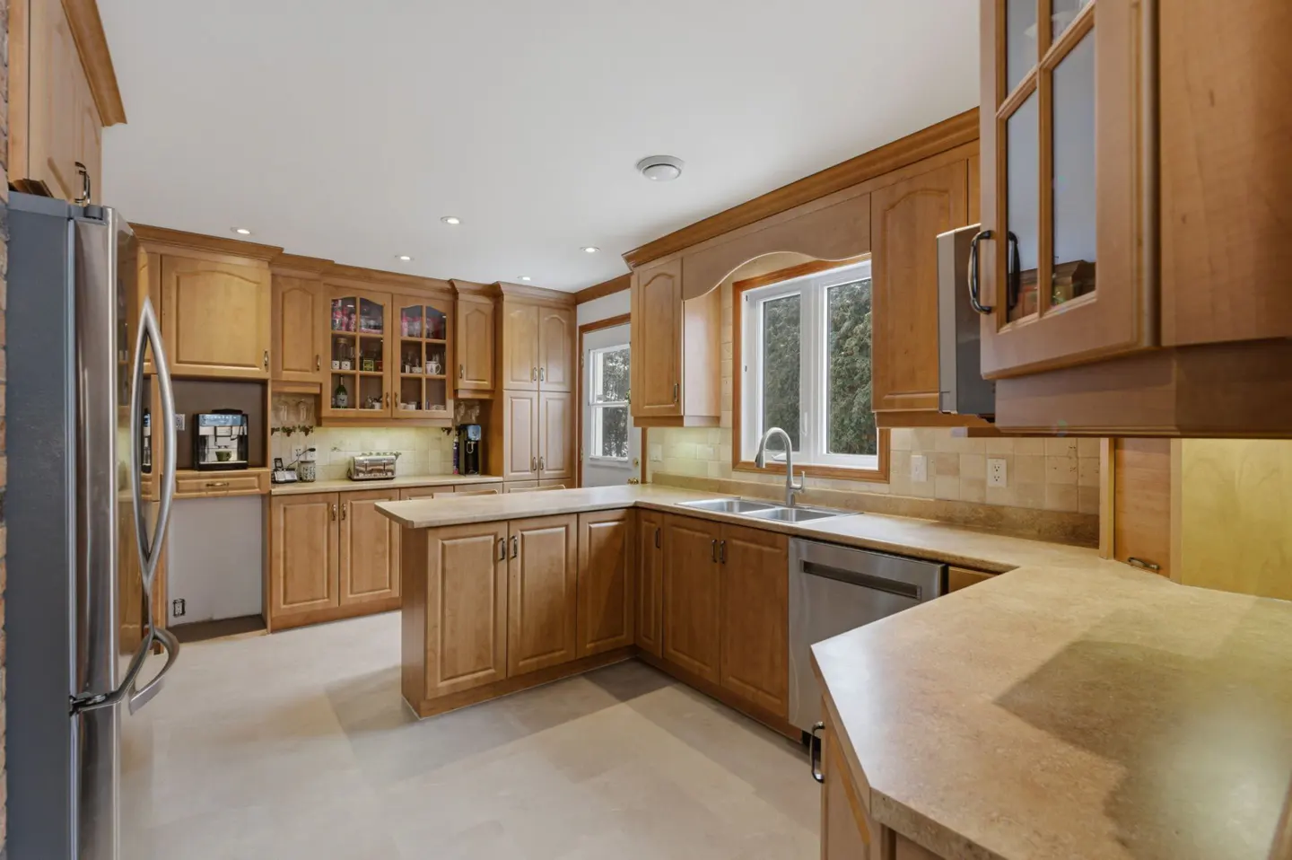 Kitchen with light wood cabinets, beige countertops, stainless steel appliances, and a window above the double sink.