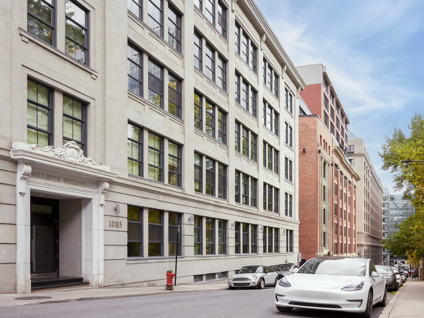 Street view of the Gillette Building at 1085, a light-colored building with many windows, and parked cars.