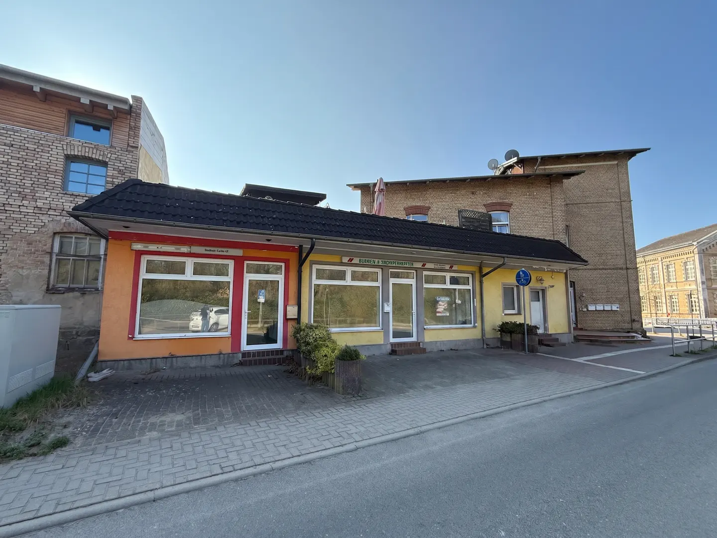 Street view of a one-story commercial building with orange and yellow facades, large windows, and a black roof.