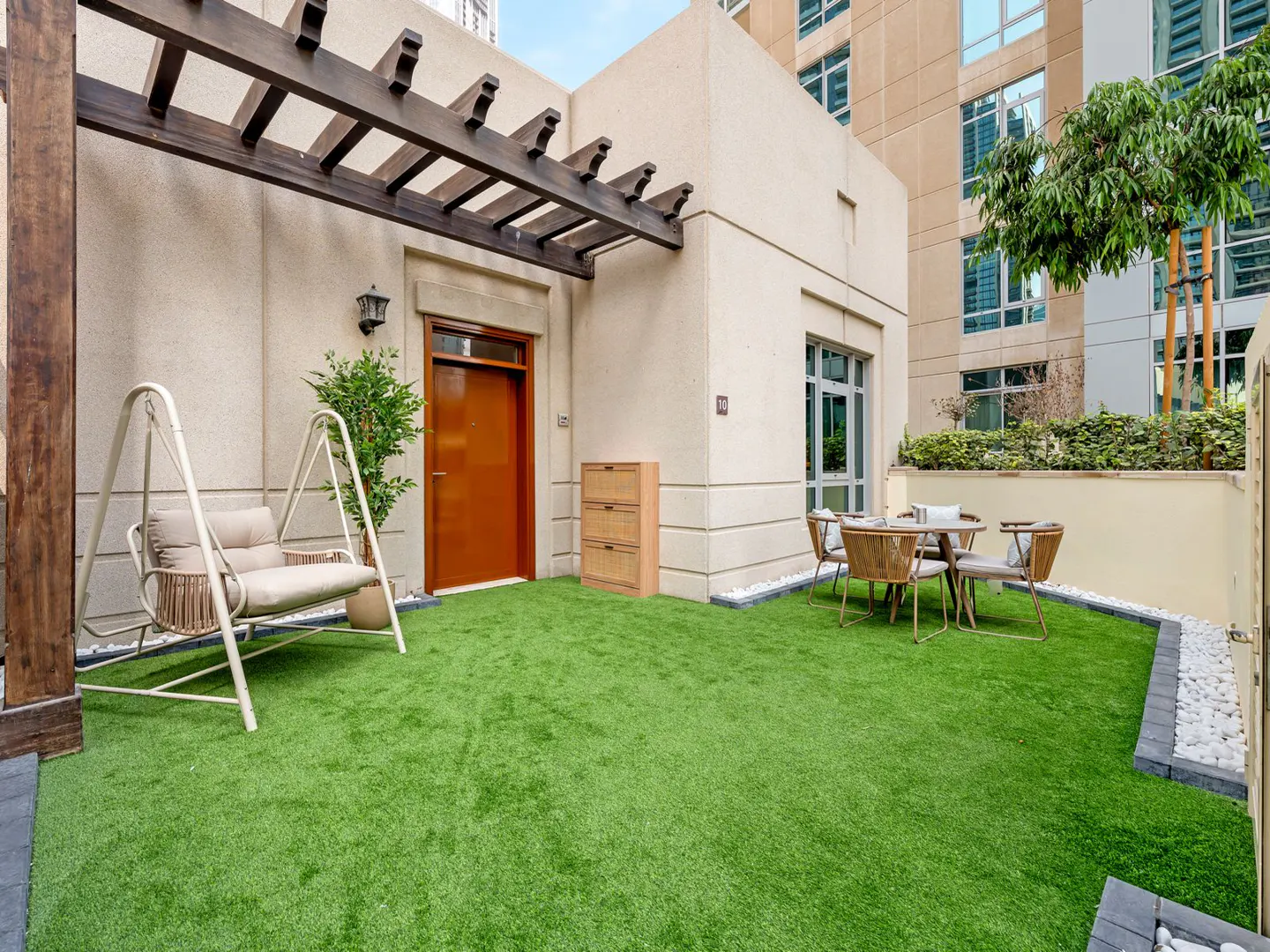 Outdoor patio with green turf, swing chair, table with four chairs, and a brown door.