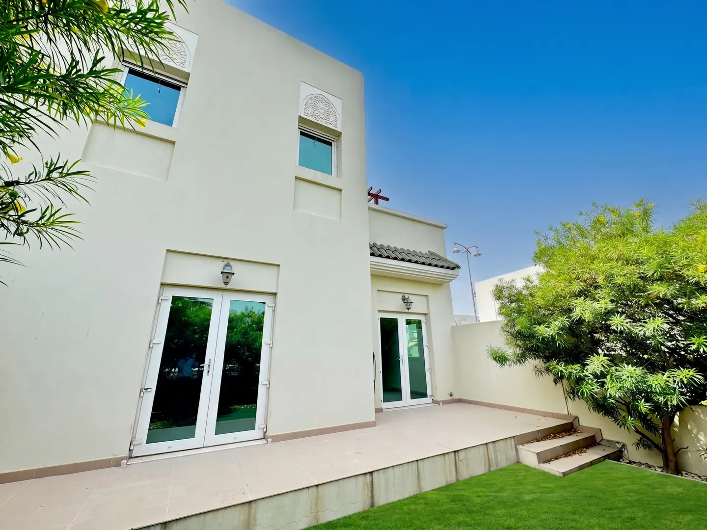 Exterior view of a two-story beige house with white trim, a patio, green grass, and a blue sky.
