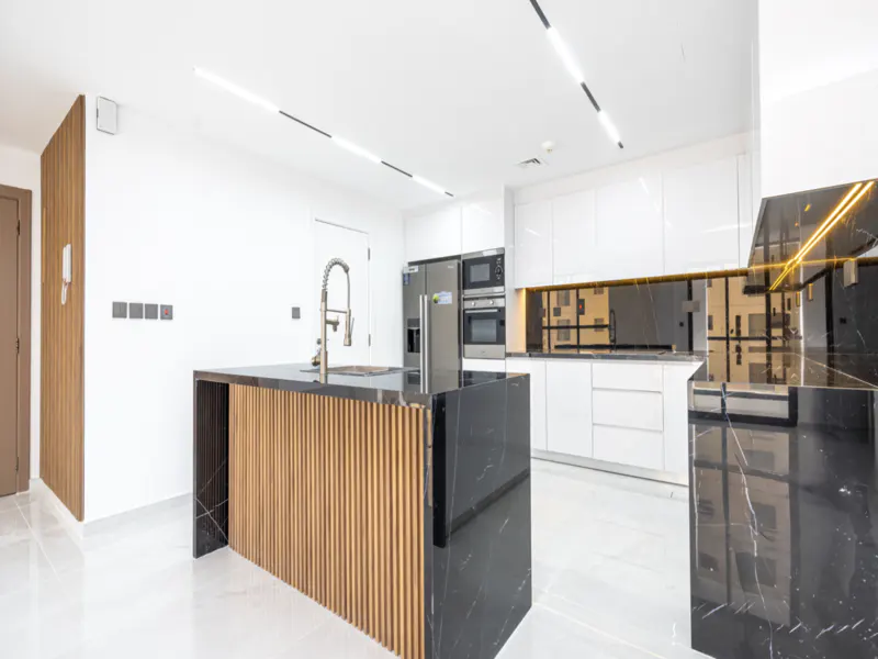 A modern kitchen with white cabinets, stainless steel appliances, and a black marble island with wood paneling.
