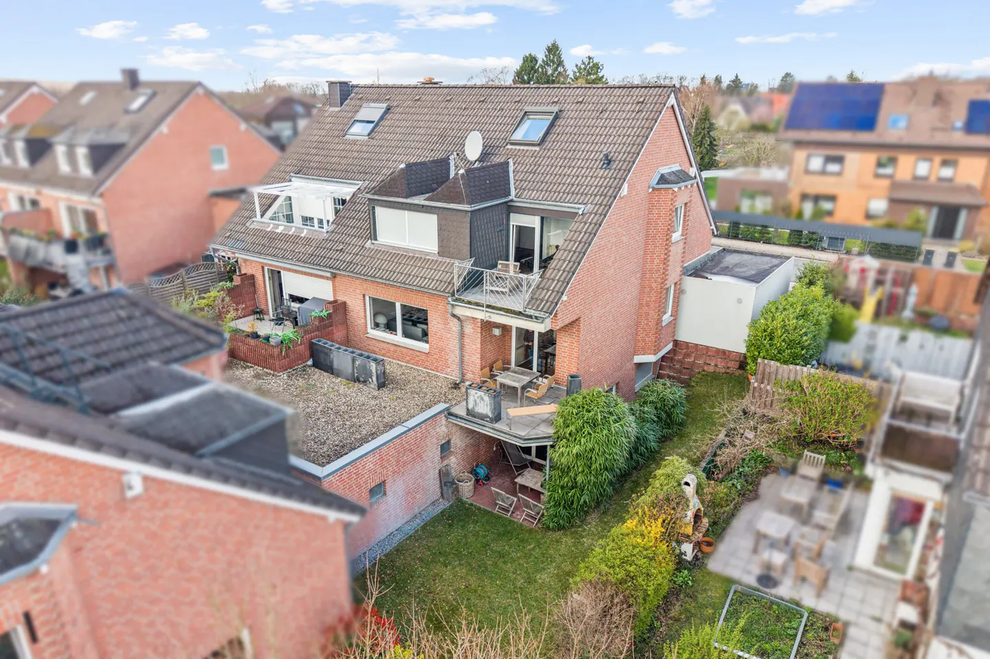 Aerial view of a red brick house with a brown roof, a balcony, and a green garden.