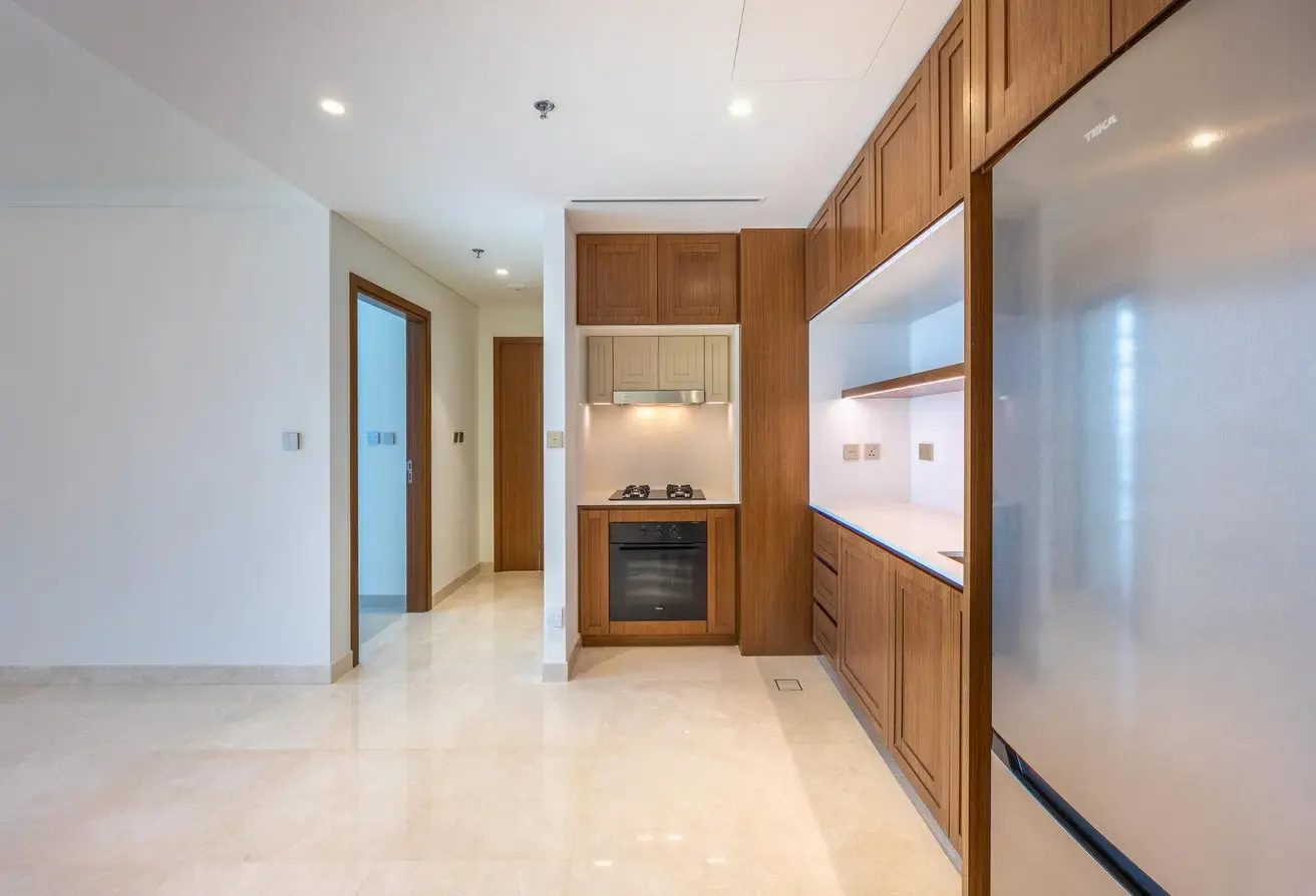 A bright, modern kitchen with wood cabinets, stainless steel appliances, and a marble floor. A hallway with wood doors is visible.