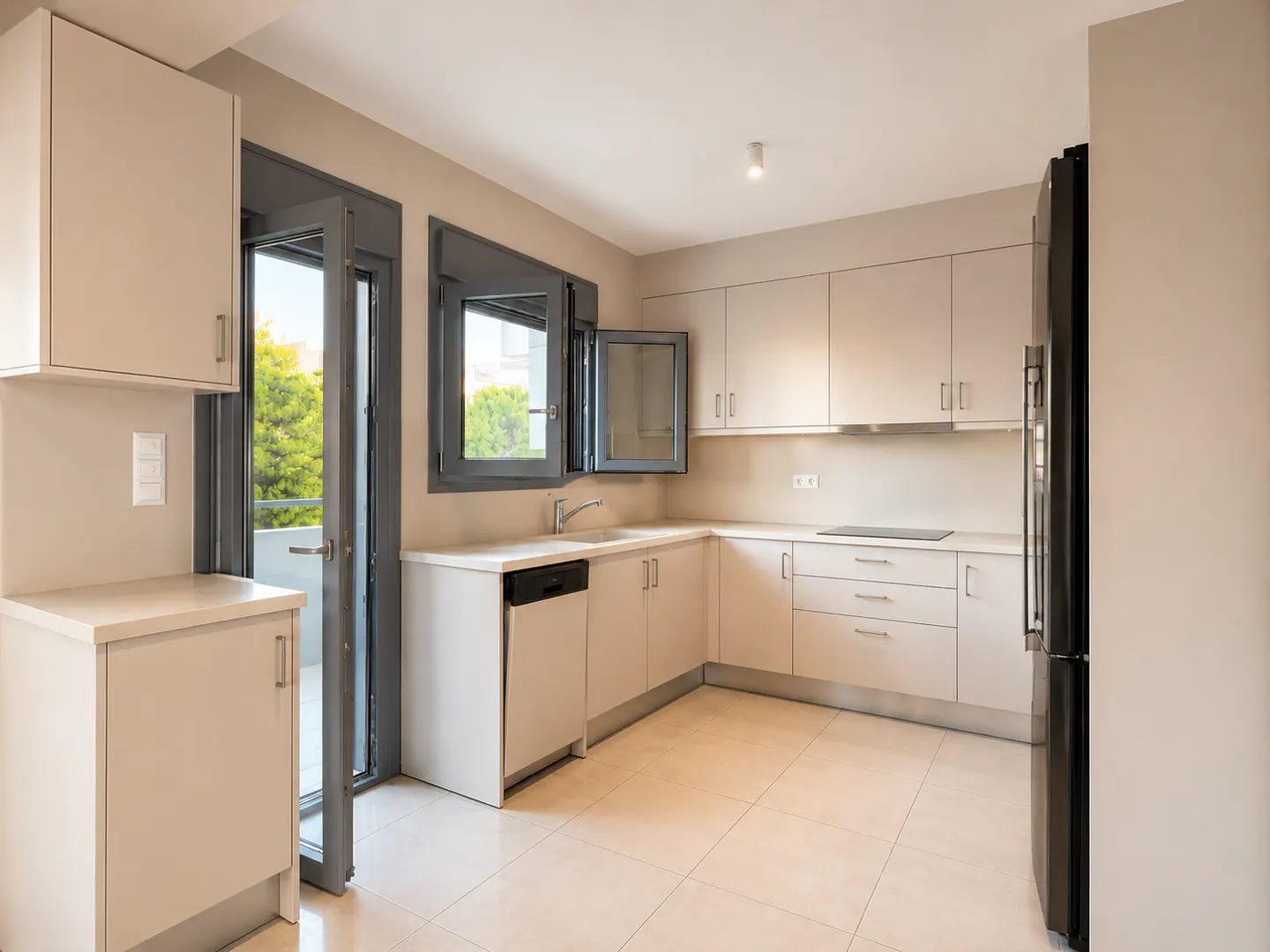 Modern kitchen with beige cabinets, light tile floors, a black refrigerator, and a door opening to a balcony.