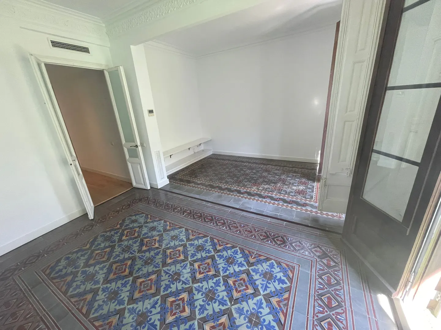 A bright room with patterned tile floors, white walls, and an open doorway to a room with a rug.