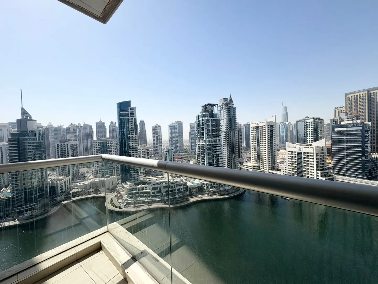 View from a high-rise balcony with a metal railing and glass panels overlooking a city skyline and a body of water.