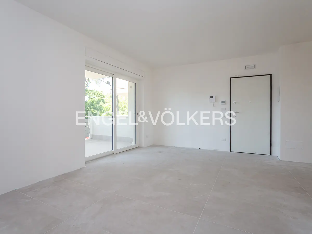 Empty, bright room with white walls, light gray tile floors, a white door, and a sliding glass door leading to a balcony.