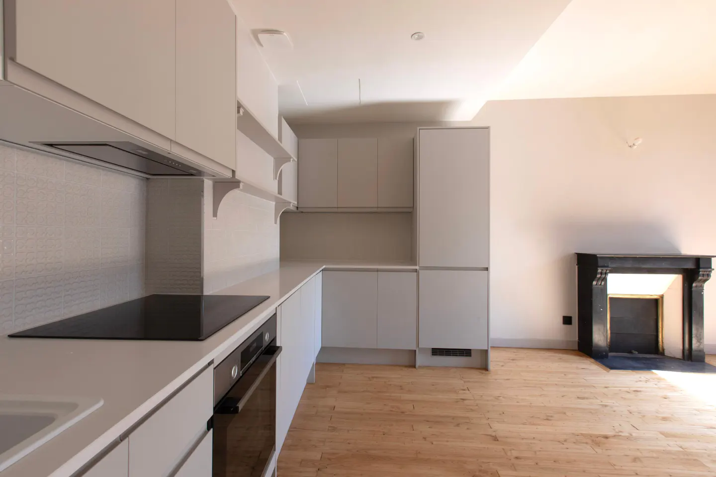 A bright kitchen with light gray cabinets, white countertops, and a black stovetop. A black fireplace is visible in the background on a wood floor.