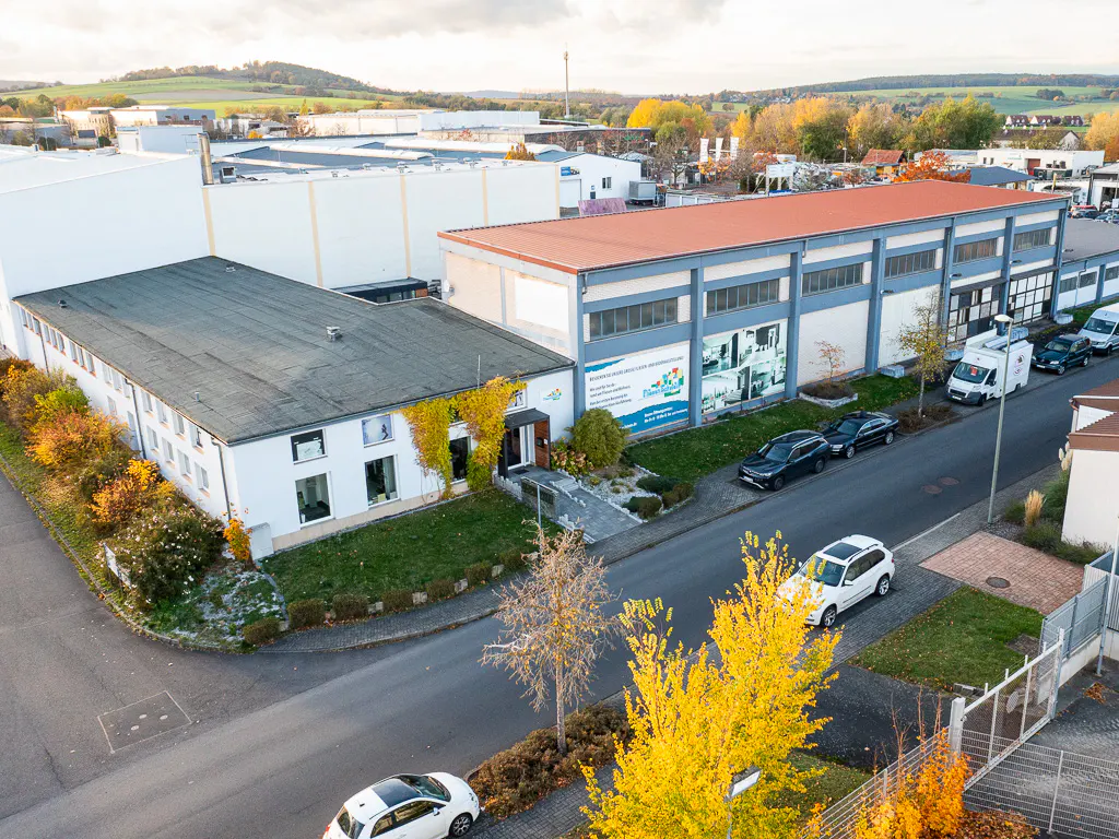 Aerial view of a commercial building with a red roof, surrounded by trees and parked cars.